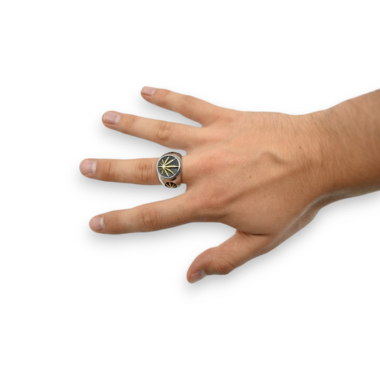 Bague chevalière argent à motif feuille de cannabis dorée, portée à la main.